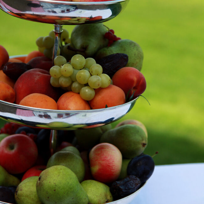 Dreistöckige Silber-Etagere gefüllt mit frischem Obst auf der Hochzeitstafel im Garten – Hochzeitsplaner Essen