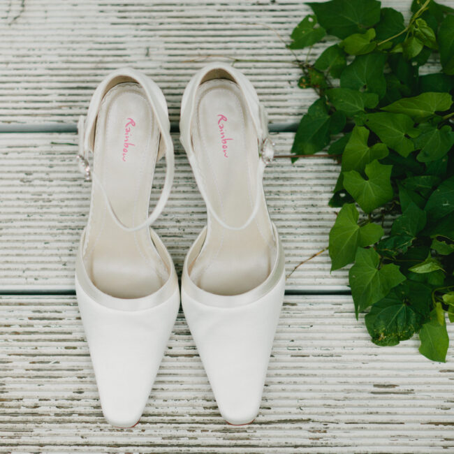 Weiße Brautschuhe mit zarten Bändchen auf Holzboden mit Efeu – Hochzeitsdetails – Hochzeitsplanung Dortmund