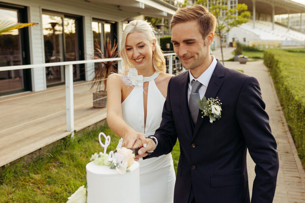 Brautpaar schneidet weiße Hochzeitstorte vor Reitbahn an – freie Trauung – Hochzeitsplanung Solingen