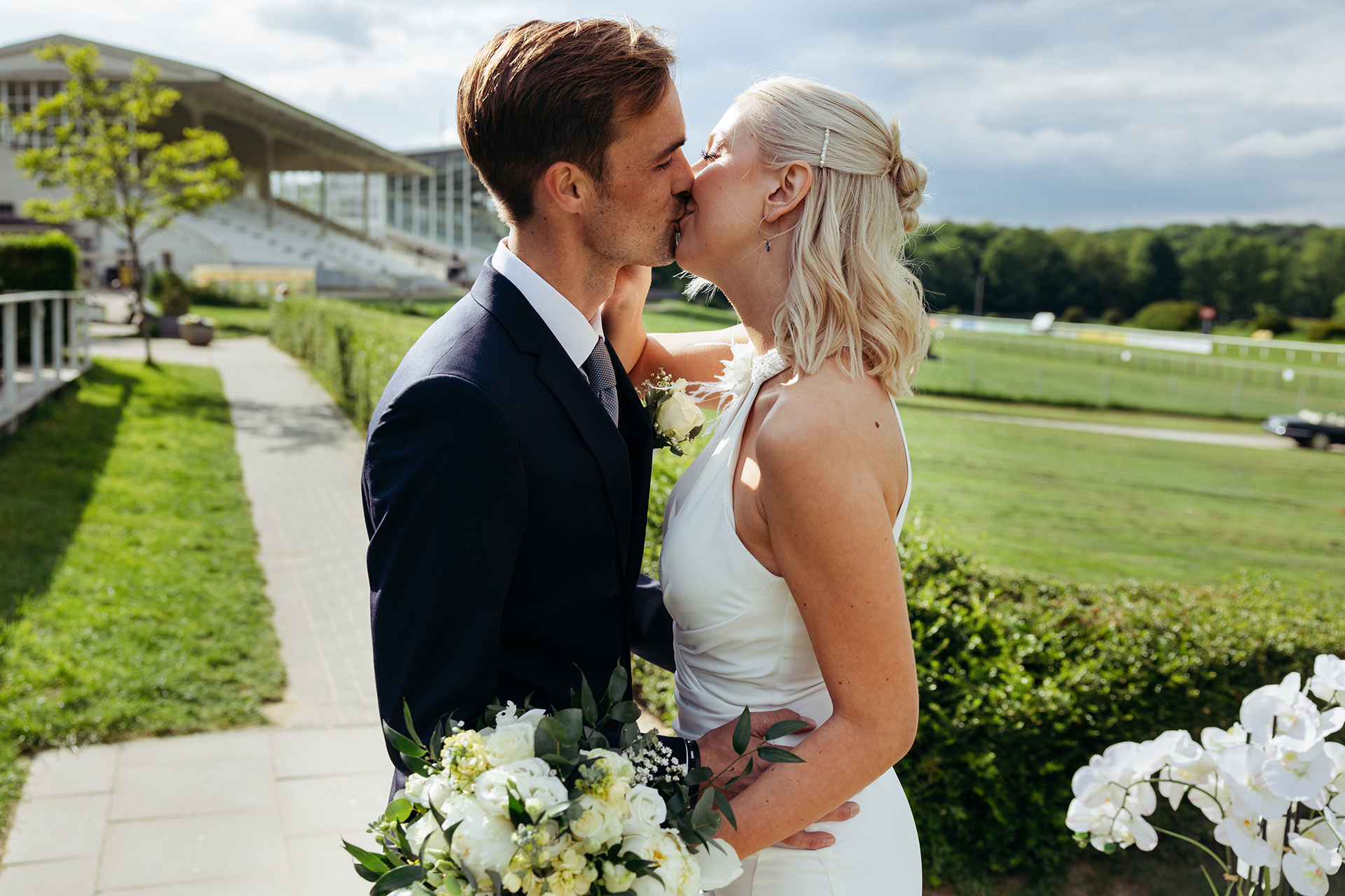 Brautpaar küsst sich mit weißem Brautstrauß vor Reitbahn – Weddingplaner Solingen